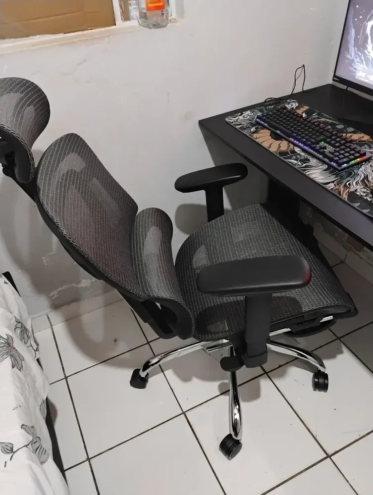 Cadeira ergonômica Mônaco BT07 Luvinco de malha cinza montada ao lado da mesa do computador